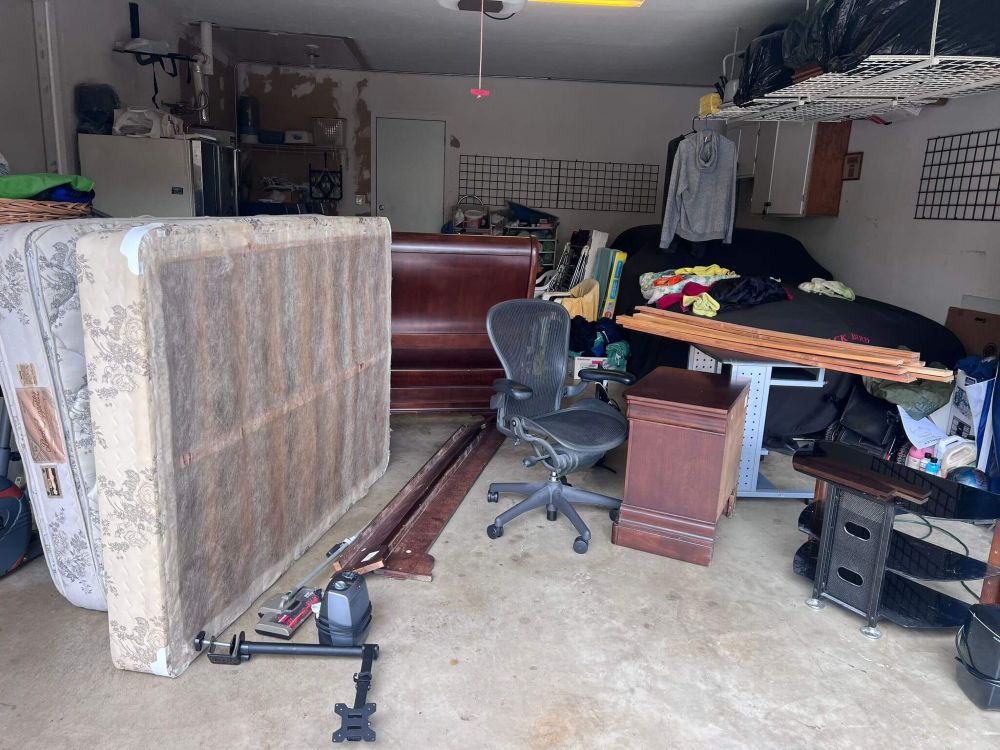 Cluttered garage filled with a mattress, office chair, wooden furniture, and assorted items, illustrating a space in need of junk removal services.